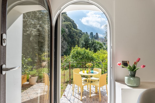 Un balcon avec une table et des chaises, un pot de fleurs et une vue sur une zone boisée.