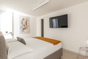 A bedroom with a bed, a TV mounted on the wall, a door, and a window. - Palazzo Ferrara - Loft With Private Garden by Wonderful Italy (Palermo)
