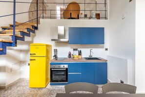 A compact kitchen with a yellow refrigerator, blue cabinets, a wooden staircase, and a view of the living area. - Palazzo Ferrara - Loft With Private Garden by Wonderful Italy (Palermo)