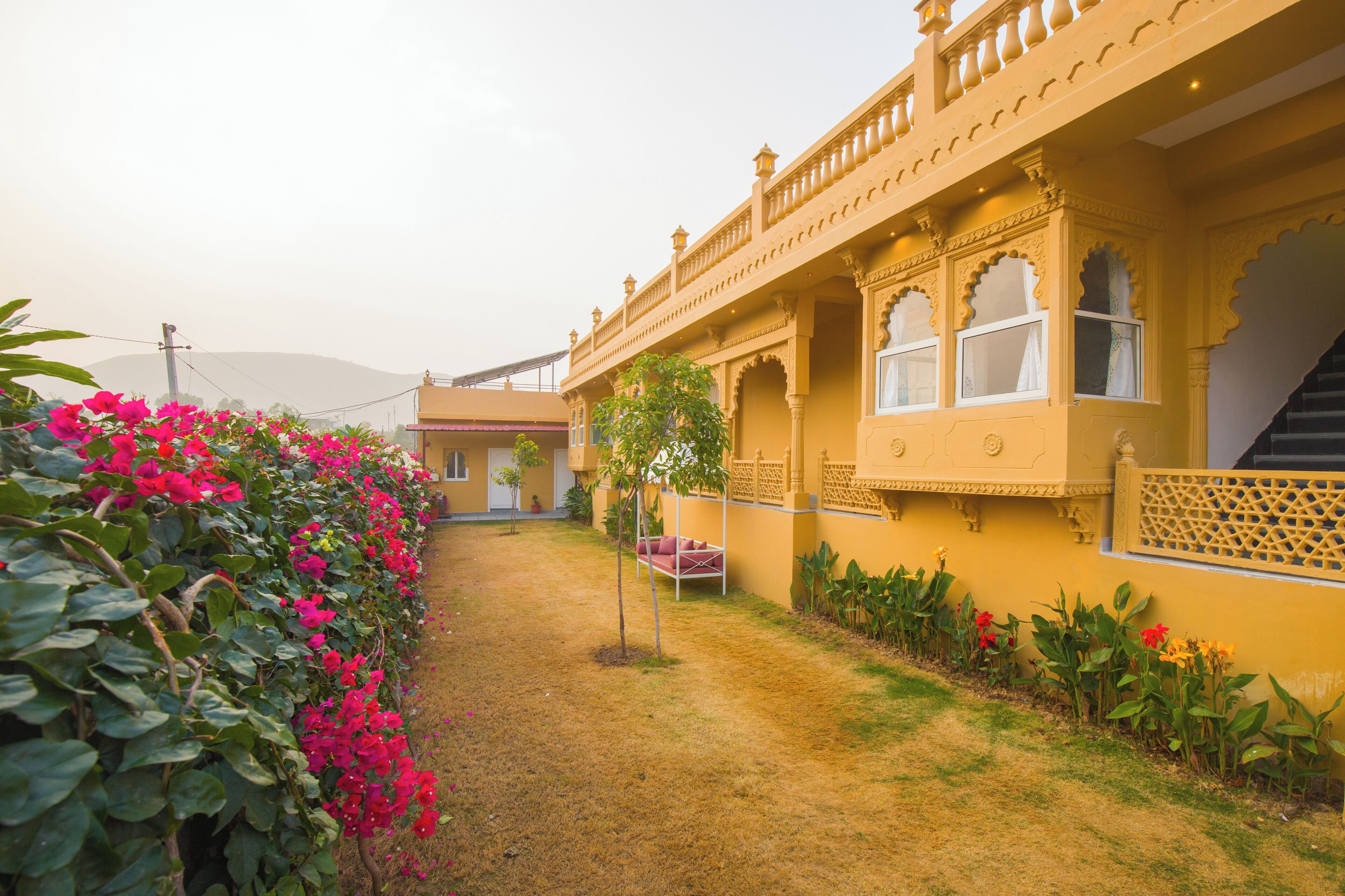 A traditional building with a courtyard, a small garden with pink flowers, and a staircase leading to the upper floors.