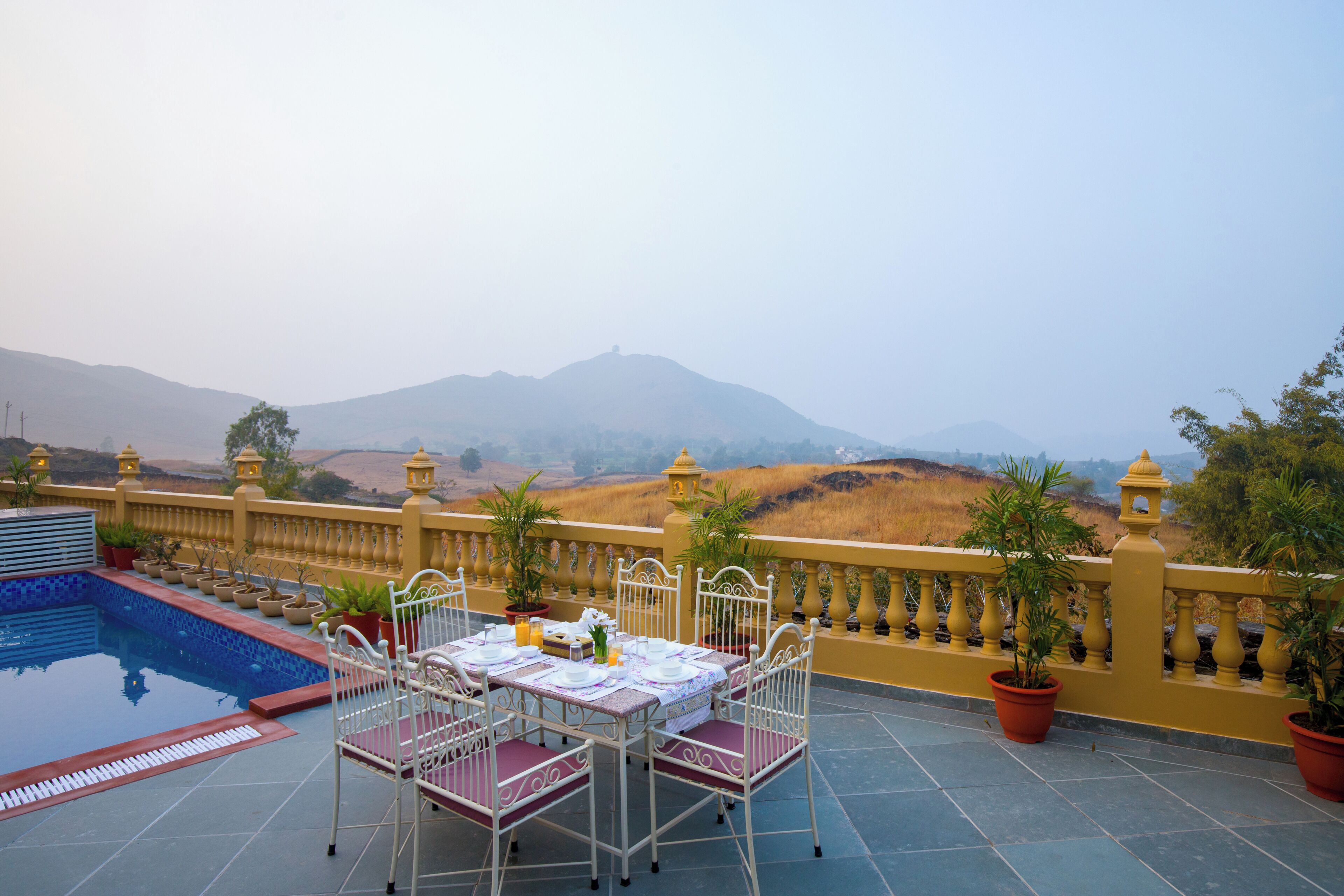 A terrace with a pool, dining table, chairs, and potted plants.
