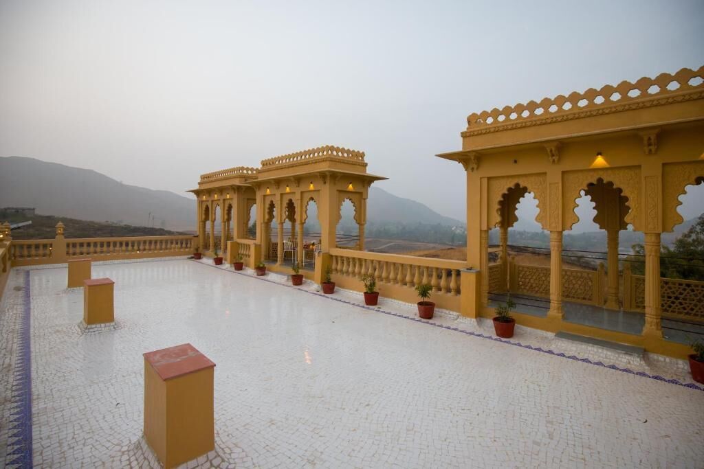 Una terrazza con strutture ornate di colore giallo, piante in vaso e montagne sullo sfondo.