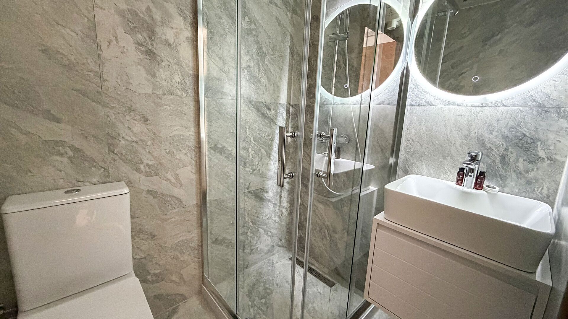 A modern bathroom with a glass-enclosed shower, a toilet, and a sink with a mirror.