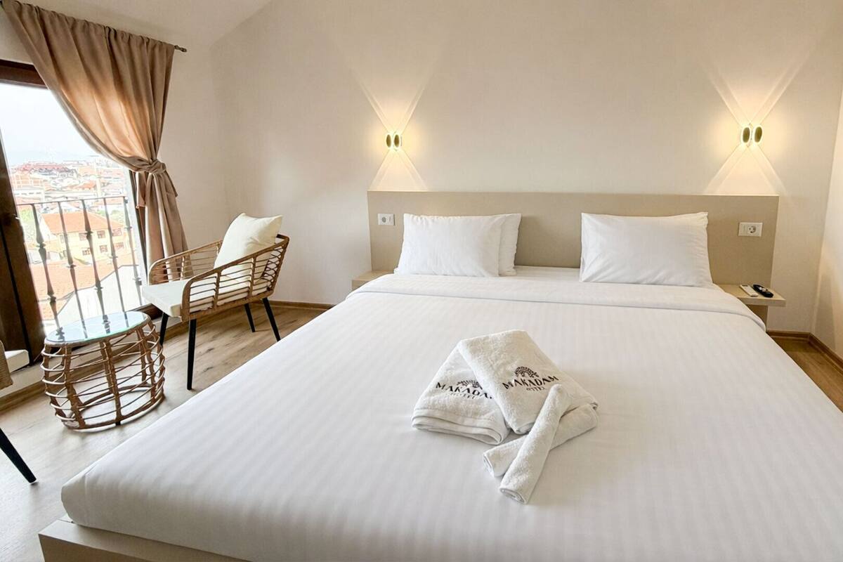 A hotel room with a large bed, two bedside tables, a chair, and a balcony view.
