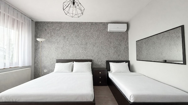 Een moderne hotelkamer met twee enkele bedden, een grote spiegel, een geometrische lamp en een gestructureerde grijze wand.