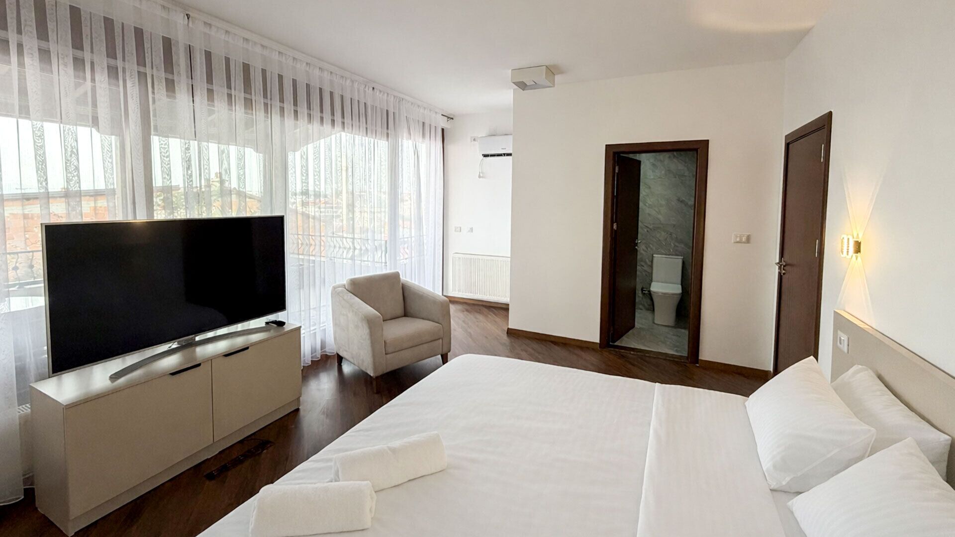 Quarto de hotel com cama, televisão, cadeira e porta do banheiro.