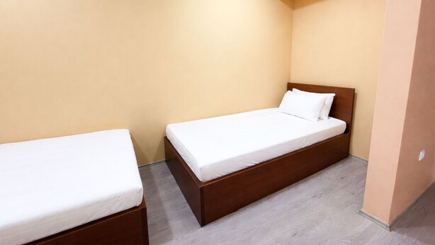 Two single beds with wooden frames and white bedding in a room with beige walls and a light-colored floor. - Makadam Hotel (Prizren)