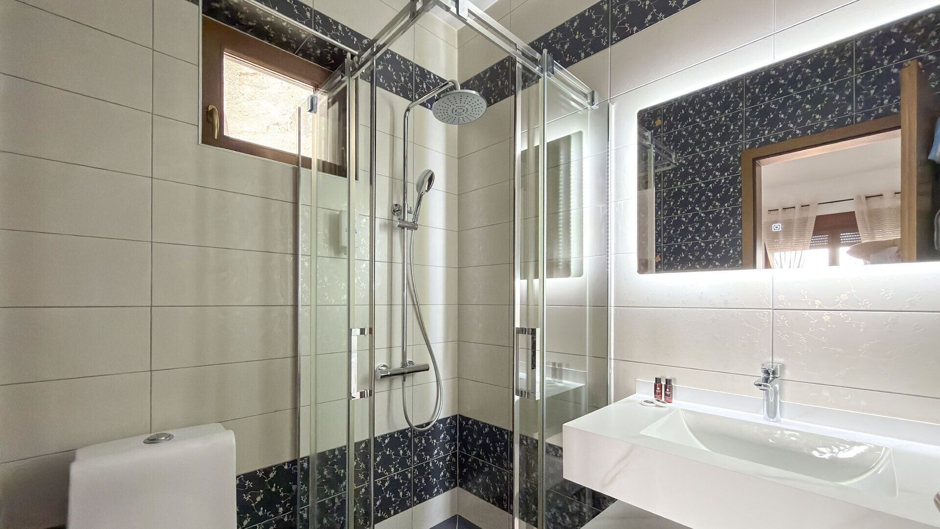 A modern bathroom with a glass shower enclosure, a white sink, and a mirror with a floral tile backsplash.