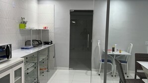 A modern kitchen with white tiles, a refrigerator, a sink, and a dining area with chairs and a table. - Hotel Santa Rita (Amarante do Maranhão)