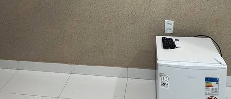 A room with a flat-screen TV mounted on the wall, a white refrigerator, and a white shelf unit.