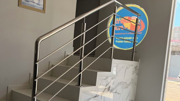 A staircase with a metal railing, marble steps, and a wall with a framed picture and a circular sign. - Hotel Santa Rita (Amarante do Maranhão)