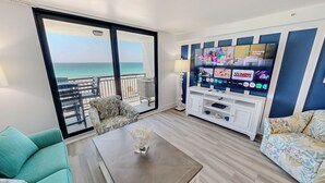 Un balcon avec vue sur la mer, un téléviseur affichant les logos de différents services de diffusion en continu et un canapé à motifs.