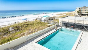 Une piscine avec vue sur la plage, un poste de surveillance pour les sauveteurs et un bâtiment doté d’un balcon.