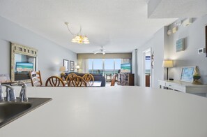 A modern living room with a large white table, a ceiling fan, and a view of the ocean through large windows. - Large 3 Bedroom Beachfront Condo - Sleeps 10! Free Seasonal Beach Service! (Fort Walton Beach)