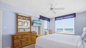 Un dormitorio con cama, cómoda, televisor, ventilador de techo y ventana con vista a la playa.
