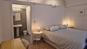 A bedroom with a bed, bedside table, lamp, and a view into the bathroom. - Ancient hermitage in the upper Langa. Experience the essence of a frontier land (Costa)