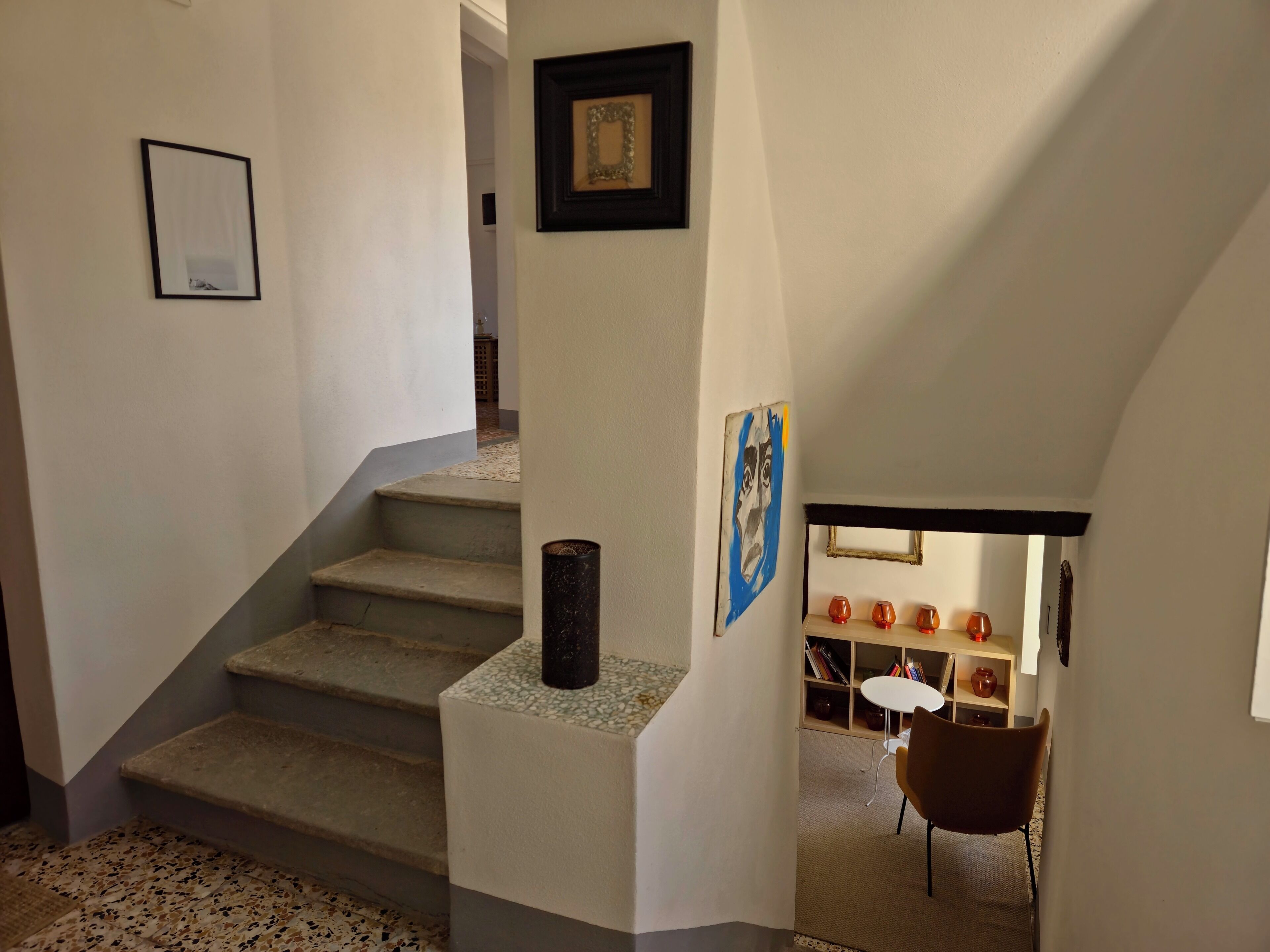 Una escalera con piso alfombrado, un cuadro en la pared y una pequeña mesa con sillas al fondo.