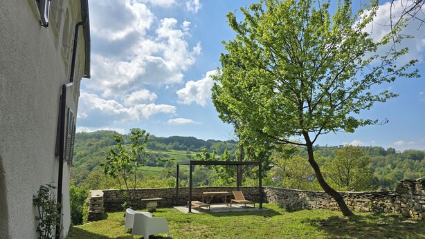 A stone wall, a wooden bench, and a tree in a grassy area with a view of a hilly landscape. - Ancient hermitage in the upper Langa. Experience the essence of a frontier land (Costa)