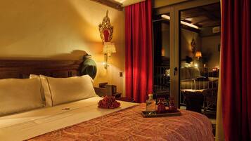 Quarto de hotel com cama, mesa de cabeceira, luminária, cortina vermelha e vista para o exterior.