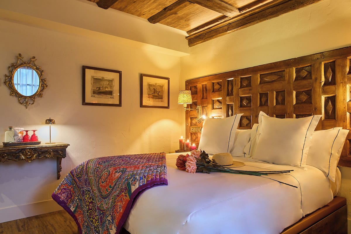 Una cama con sábanas blancas, un edredón colorido y un cabecero de madera.