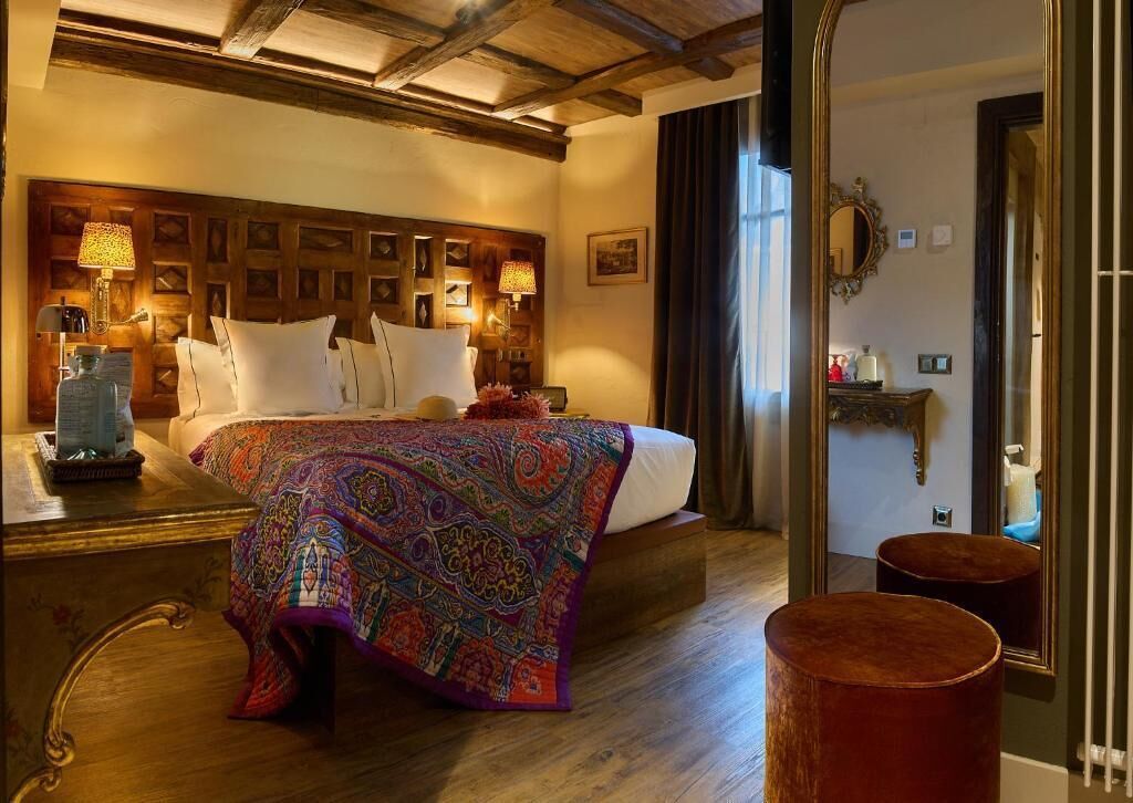 A hotel room with a wooden headboard, a patterned bedspread, a nightstand with a lamp, and a mirror on the wall.