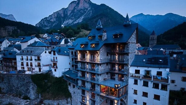 A multi-story building with balconies, a stone facade, and a mountain backdrop. - Hotel Valle de Pineta (Bielsa)