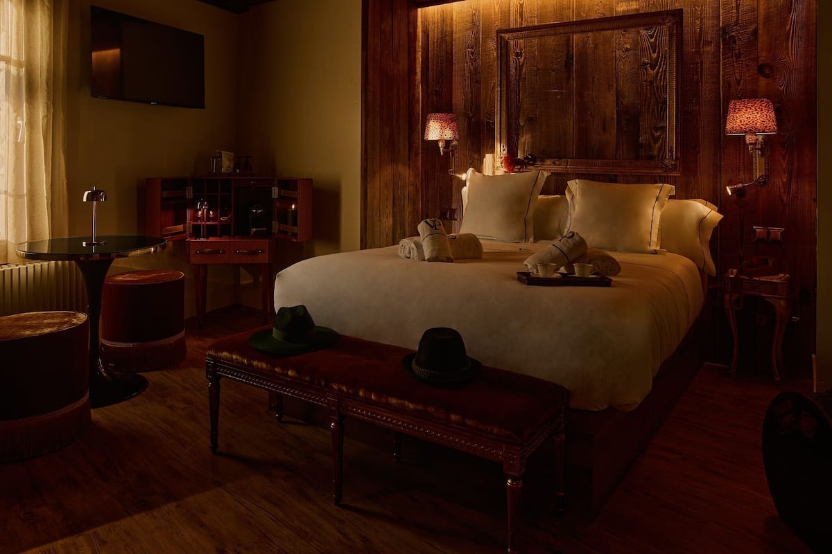 Una habitación de hotel acogedora con una cama grande, paneles de madera, televisor, escritorio y lámpara.