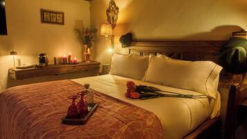 Una cama bien hecha con una colcha estampada, una mesita de noche con lámpara, velas y un jarrón con flores.