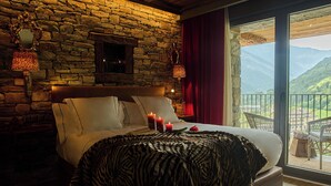 A bedroom with a stone wall, a bed with white linens, two wall sconces, and a view of mountains through a large window. - Hotel Valle de Pineta (Bielsa)