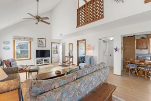 A spacious living room with a sofa, television, and wooden dining table. - Just Beachy: Short walk to Beach | Hot Tub (Waves)