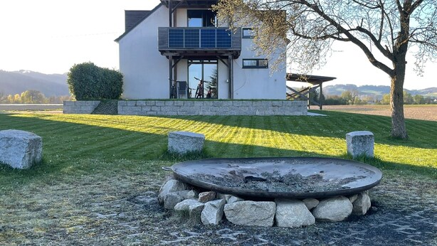 Ein modernes Haus mit Solaranlage, Kiesfeuerstelle und gepflegtem Rasen.