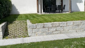 Ein modernes Gebäude mit einer Terrasse, die Gartenmöbel und eine Mauer aus Naturstein umfasst.