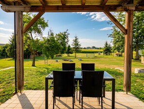 An outdoor patio with a table and chairs, surrounded by a wooden pergola, overlooking a grassy area with trees and a distant view of a field. - Apartment “LandSuite Schaunbergblick” with Private Terrace and Wi-Fi (Au bei Brandstatt)