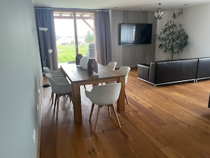 Un salon moderne comprenant un coin repas, un téléviseur à écran plat fixé au mur et une grande fenêtre avec des rideaux.