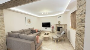 Ein modernes Wohnzimmer mit Sofa, Sessel, Couchtisch, Fernseher, Kamin und Wandverkleidung aus Stein.