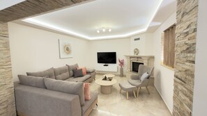 Ein modernes Wohnzimmer mit Sofa, Sessel, Couchtisch, Fernseher, Kamin und Wandverkleidung aus Stein.