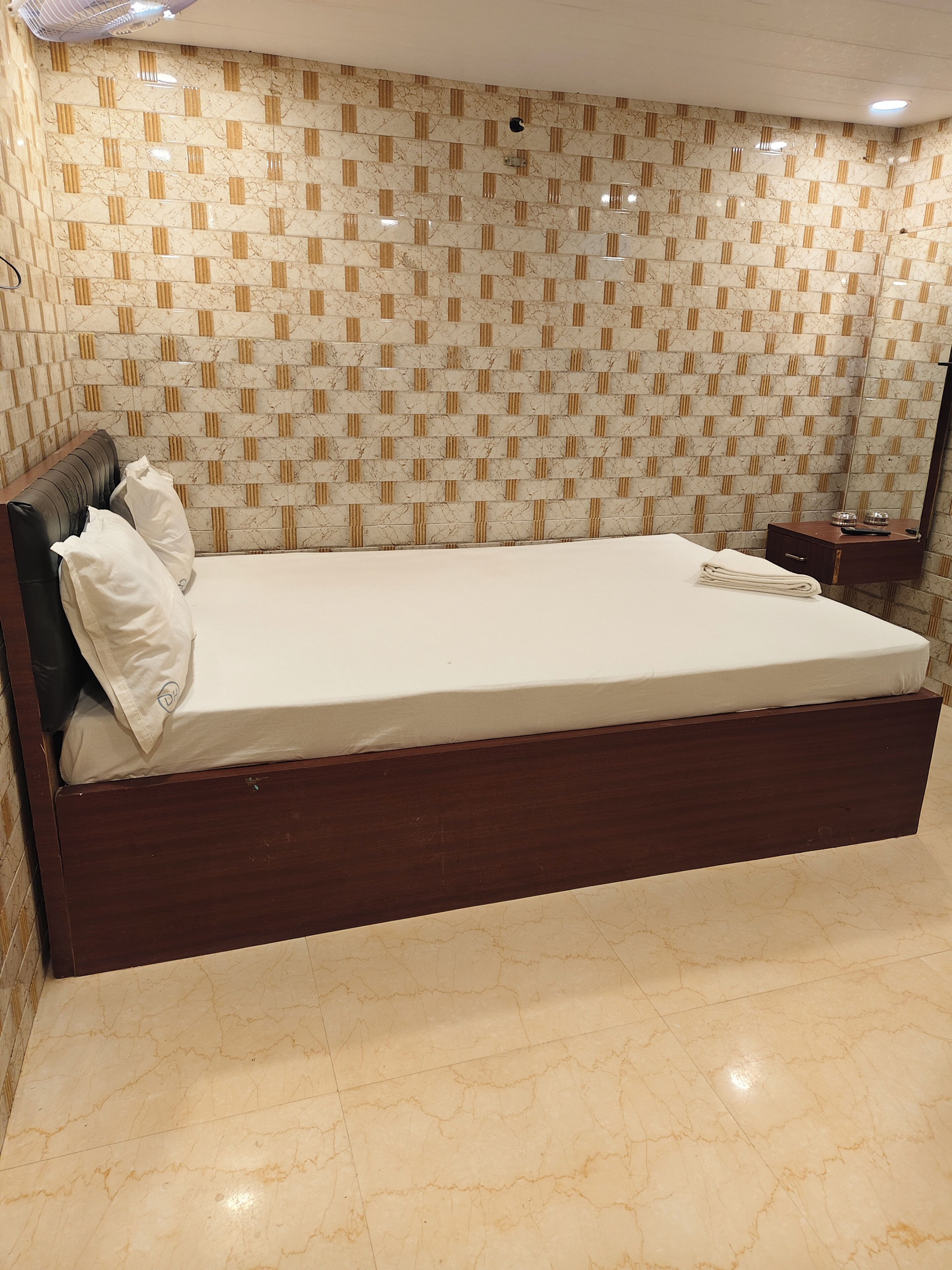 A bedroom with a large bed, a wooden headboard, a nightstand, a mirror, and a patterned wall.