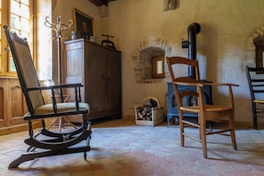 A room with a wooden rocking chair, a wooden chair, a fireplace, and a cabinet. - Gite in the heart of a former priory - quiet, leafy setting (Ruffey-sur-Seille)