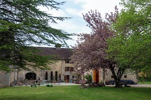 A stone building with a courtyard, outdoor seating, and a tree with purple blossoms. - Gite in the heart of a former priory - quiet, leafy setting (Ruffey-sur-Seille)