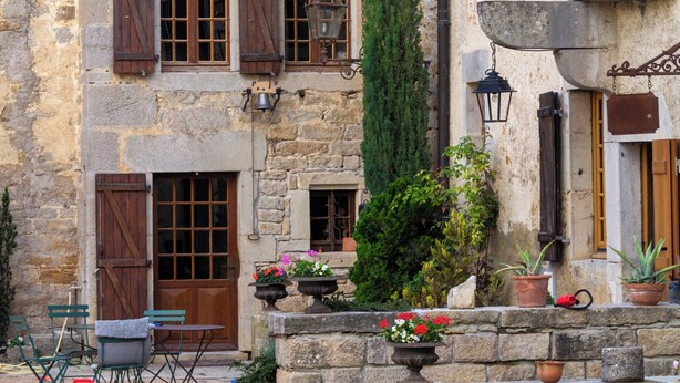 Un edificio de piedra con múltiples ventanas, un balcón y asientos al aire libre.