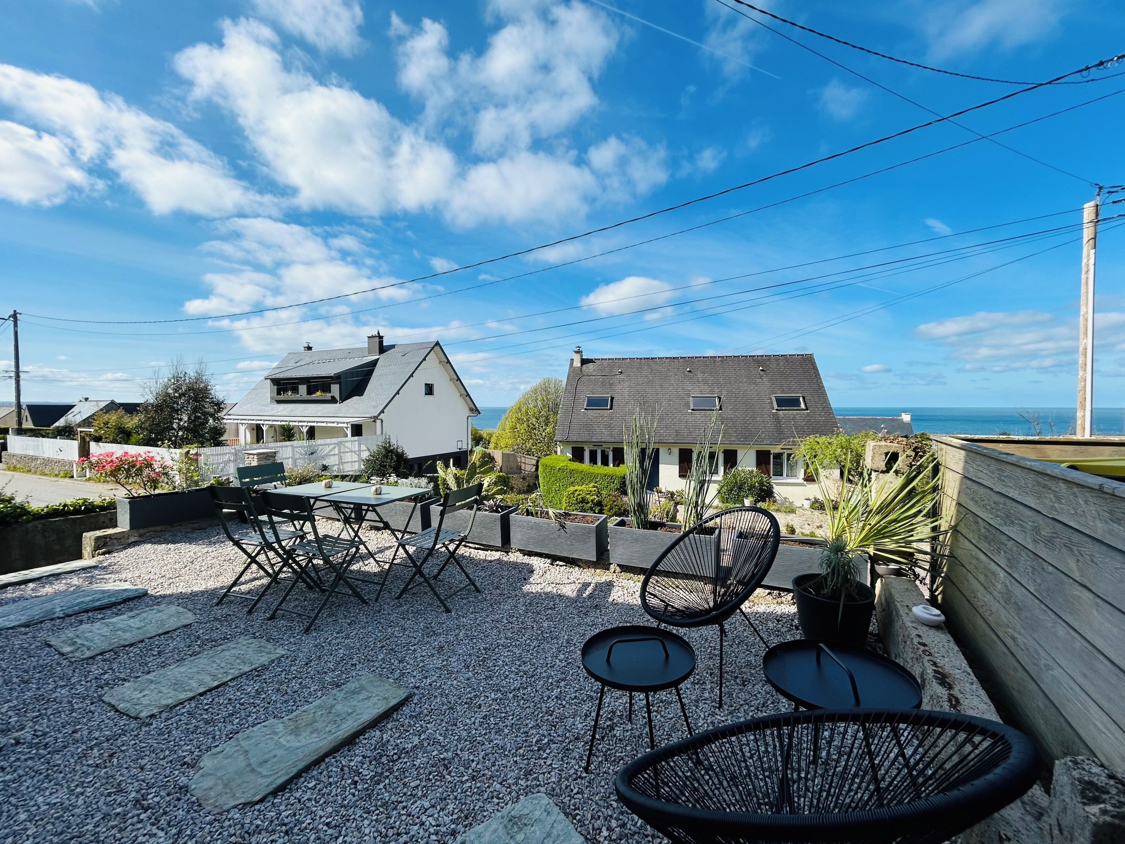 Une terrasse avec des meubles d’extérieur, une maison blanche et une maison grise avec vue sur la mer.