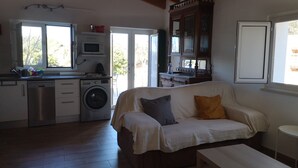 Ein kompakter Wohnraum mit Küchenzeile, Waschmaschine, einer Couch mit Kissen und einem Esstisch.