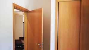 Ein Zimmer mit Holztür, einem Bett und einem Essbereich, der durch eine geöffnete Tür sichtbar ist.