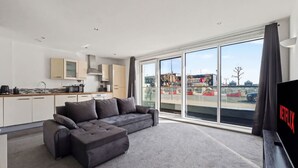 Una sala de estar moderna con un sofá gris, una zona de cocina y un ventanal con vistas al exterior.