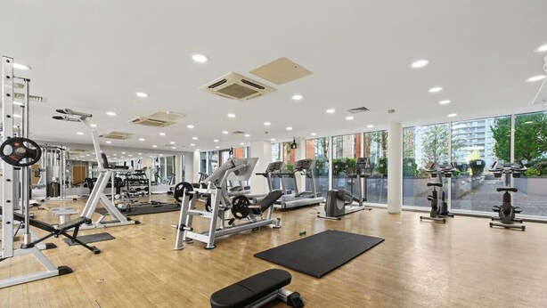 Un gimnasio con máquinas de cardio, equipo de levantamiento de pesas y un amplio ventanal con vistas al exterior.