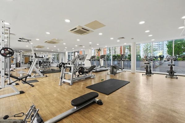 A gym with cardio machines, weightlifting equipment, and a large window providing a view of the outside. - ExCel & O2 Waterfront Apartment with Gym Access (Greater London)
