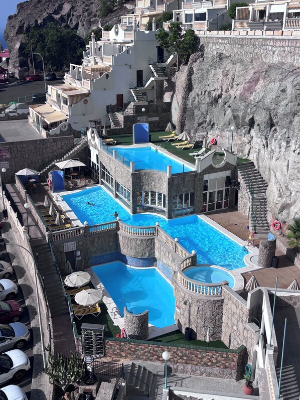 A multi-level swimming pool complex with stone architecture, multiple levels of balconies, and a view of the surrounding rocky landscape. - Vista Mar - Playa del cura (Mogán)