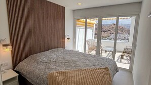 A bedroom with a large bed, a wooden slat wall, a small bedside table, and a view of the outdoors through a sliding glass door. - Vista Mar - Playa del cura (Mogán)