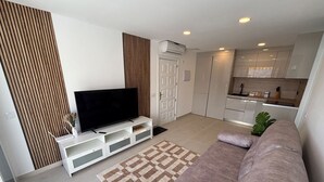 A modern living room with a flat-screen TV, a sofa, a patterned rug, and a kitchen area with cabinets and a countertop. - Vista Mar - Playa del cura (Mogán)
