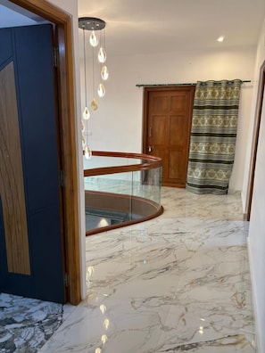 Un intérieur au sol en marbre, agrémenté d’une balustrade en verre, d’une porte en bois et d’un rideau à motifs.